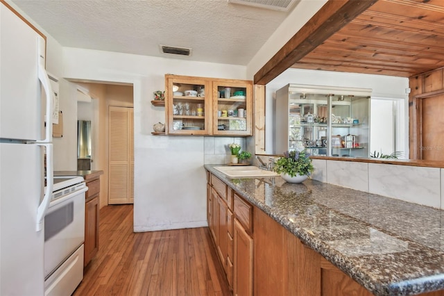 kitchen with white appliances, sink, hardwood / wood-style flooring, wooden ceiling, and dark stone countertops