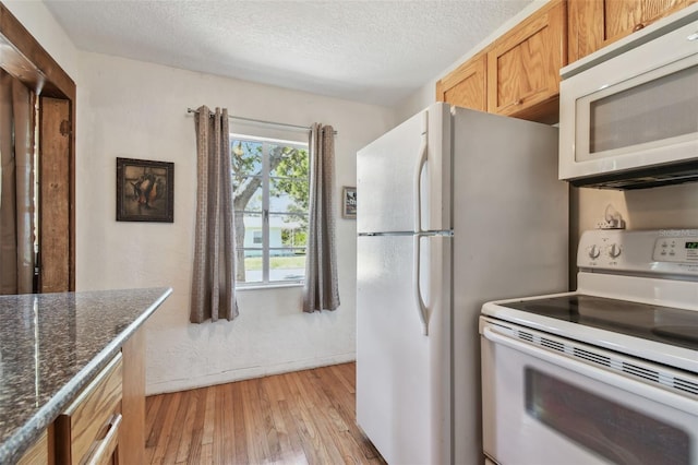 kitchen with light wood-type flooring, white appliances, a textured ceiling, and dark stone counters