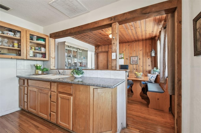 kitchen featuring kitchen peninsula, light wood-type flooring, sink, wooden ceiling, and wood walls