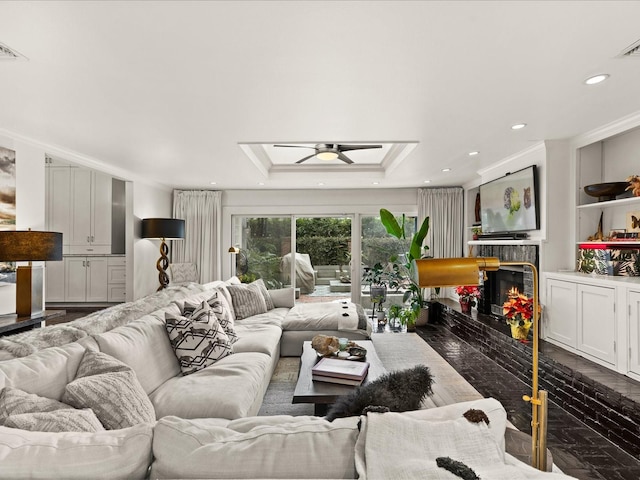 living room with a tray ceiling, a tile fireplace, ceiling fan, and ornamental molding