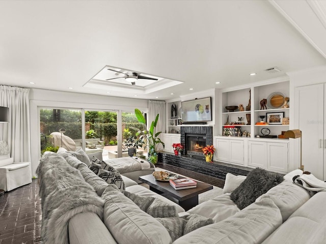 living room with ceiling fan, a raised ceiling, crown molding, and a brick fireplace