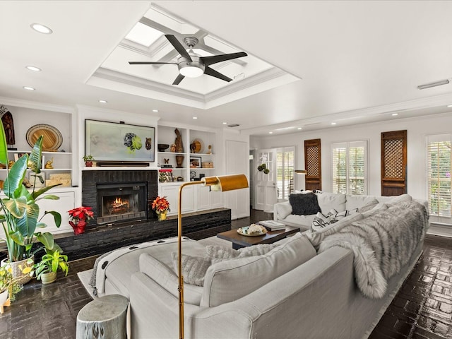 living room featuring dark parquet flooring, ceiling fan, crown molding, a tray ceiling, and a fireplace