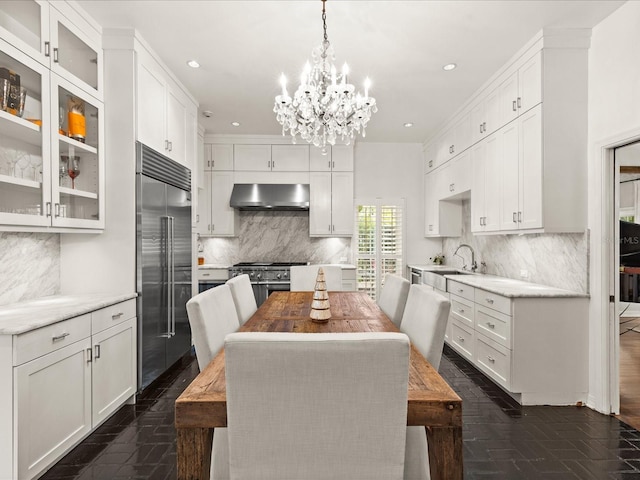 kitchen featuring white cabinetry, premium appliances, range hood, decorative light fixtures, and a kitchen island