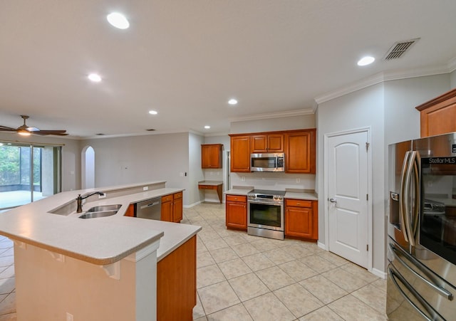 kitchen featuring a kitchen island with sink, a breakfast bar area, appliances with stainless steel finishes, crown molding, and ceiling fan