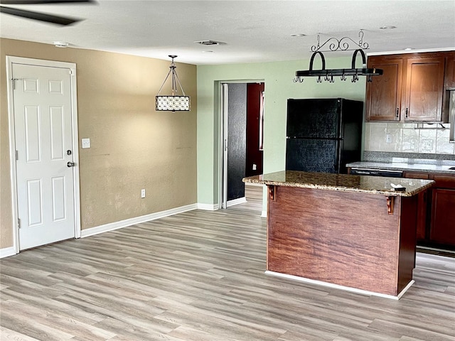 kitchen with black appliances, dark stone countertops, a kitchen island, hanging light fixtures, and a breakfast bar area