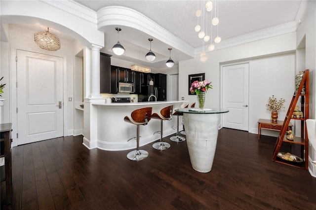 kitchen featuring a breakfast bar area, kitchen peninsula, decorative columns, and decorative light fixtures