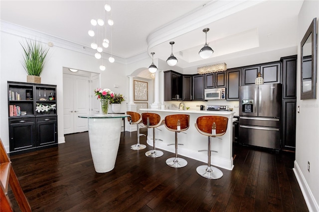 kitchen featuring pendant lighting, a raised ceiling, a breakfast bar, stainless steel appliances, and ornate columns