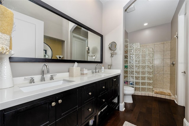 bathroom with toilet, vanity, wood-type flooring, and tiled shower