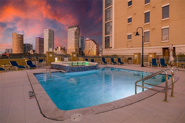 pool at dusk featuring a patio area and a hot tub