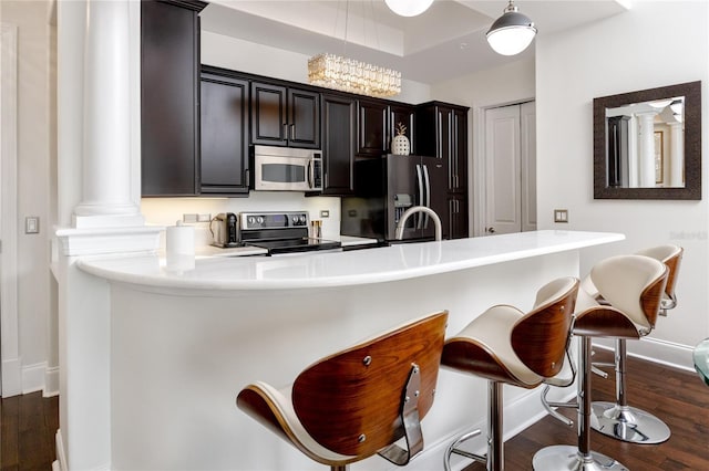 kitchen featuring stainless steel appliances, decorative light fixtures, dark hardwood / wood-style flooring, a chandelier, and a breakfast bar