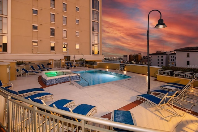 pool at dusk featuring a hot tub and a patio