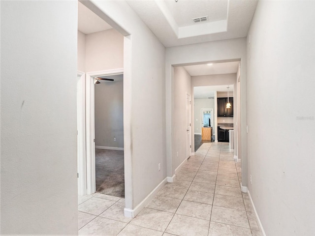 hall with a raised ceiling and light tile patterned floors