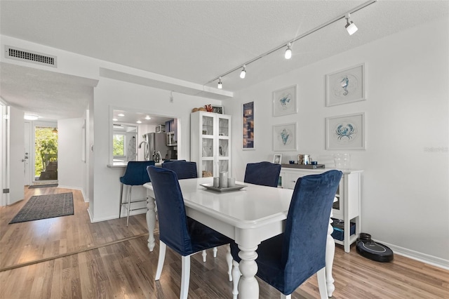 dining area with rail lighting, a textured ceiling, and light hardwood / wood-style flooring