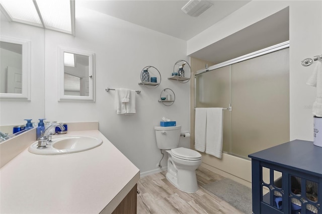 full bathroom with hardwood / wood-style flooring, toilet, vanity, and combined bath / shower with glass door