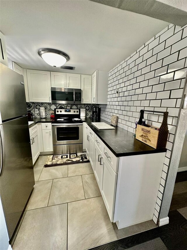 kitchen with appliances with stainless steel finishes, backsplash, white cabinetry, and light tile patterned floors