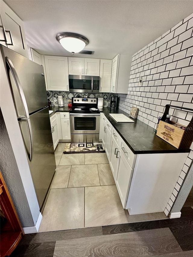 kitchen featuring light tile patterned floors, white cabinetry, backsplash, and appliances with stainless steel finishes