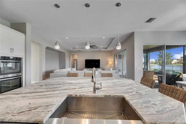 kitchen featuring double oven, light stone countertops, a tray ceiling, and sink