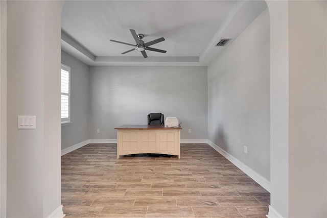 unfurnished office with ceiling fan, light hardwood / wood-style flooring, and a raised ceiling