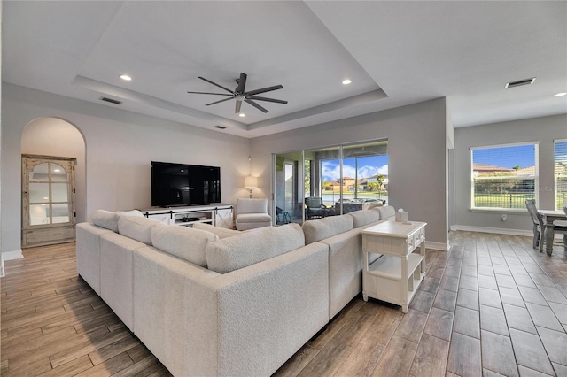 living room featuring ceiling fan, plenty of natural light, and a tray ceiling