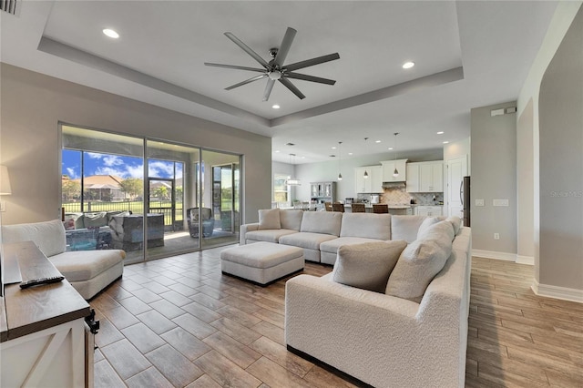 living room with a raised ceiling and ceiling fan