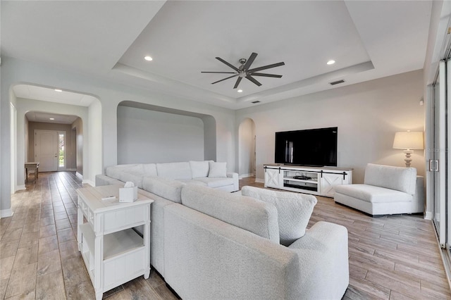 living room with a raised ceiling and ceiling fan