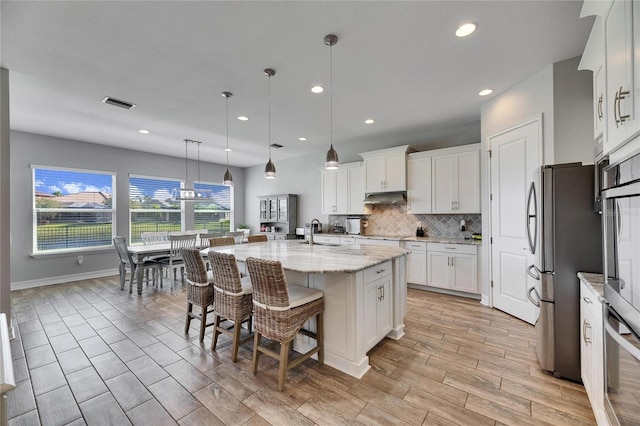 kitchen with light stone countertops, white cabinetry, decorative light fixtures, and an island with sink