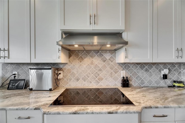 kitchen featuring white cabinets, black electric stovetop, wall chimney range hood, and tasteful backsplash