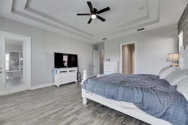 bedroom with ceiling fan, a tray ceiling, and light hardwood / wood-style flooring