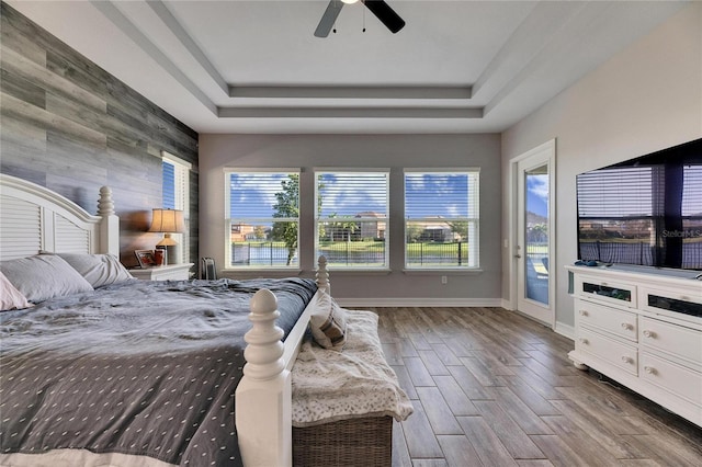 bedroom with a raised ceiling, wood walls, ceiling fan, and access to outside