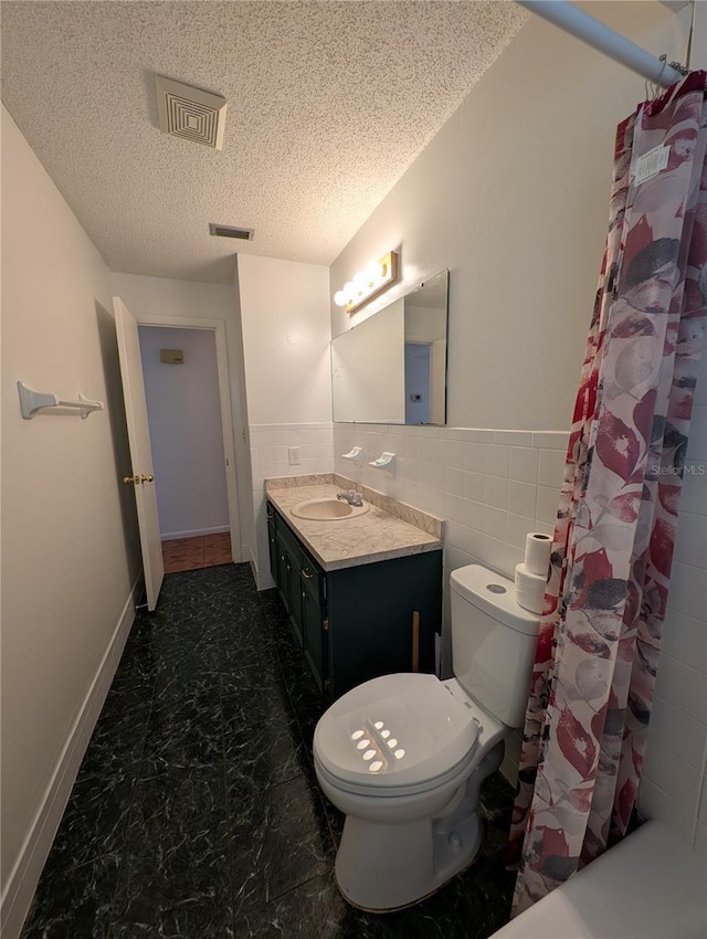 bathroom with a textured ceiling, curtained shower, vanity, and tile walls