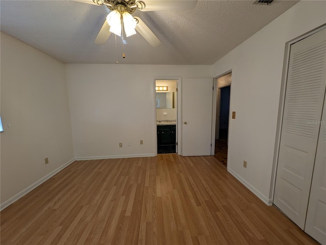 unfurnished bedroom with ceiling fan, a textured ceiling, connected bathroom, and light hardwood / wood-style flooring