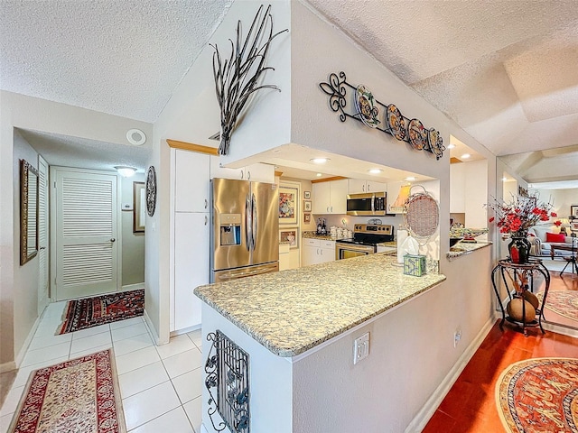 kitchen with kitchen peninsula, white cabinets, lofted ceiling, and appliances with stainless steel finishes