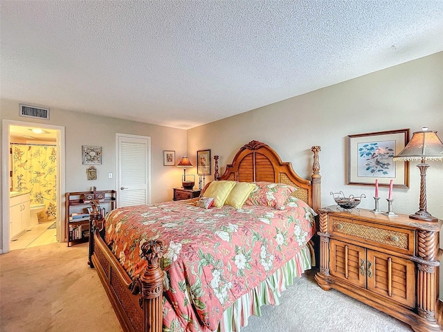 bedroom with a textured ceiling, light colored carpet, a closet, and connected bathroom