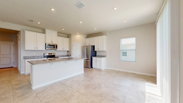 kitchen featuring a center island with sink, light stone countertops, light tile patterned flooring, white cabinetry, and stainless steel appliances