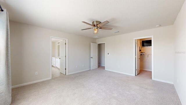 unfurnished bedroom featuring light carpet, ensuite bath, ceiling fan, a spacious closet, and a closet