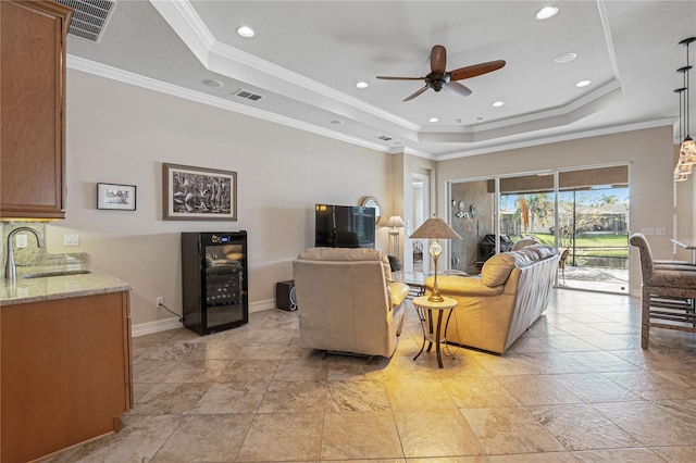 living room featuring a tray ceiling, crown molding, sink, and beverage cooler