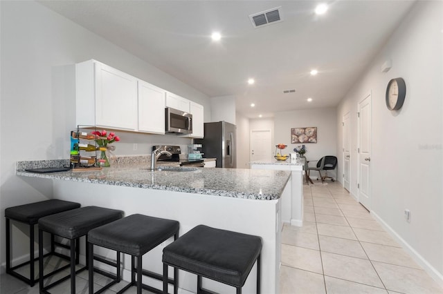 kitchen with kitchen peninsula, light stone counters, stainless steel appliances, light tile patterned floors, and white cabinets