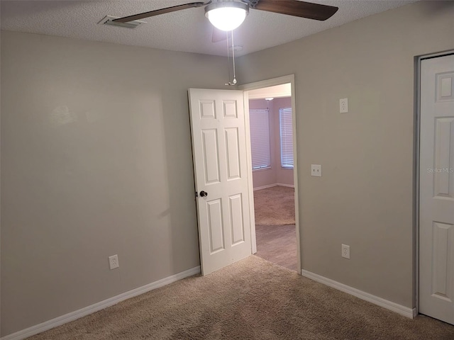 spare room with a textured ceiling, ceiling fan, and light colored carpet