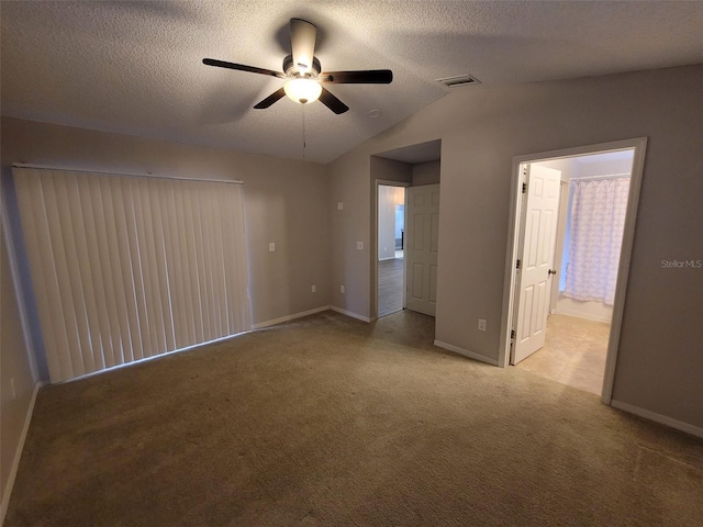 carpeted empty room featuring ceiling fan, a textured ceiling, connected bathroom, and lofted ceiling