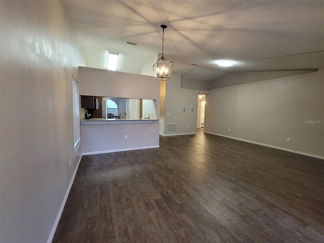 unfurnished living room featuring a textured ceiling, dark wood-type flooring, lofted ceiling, and a notable chandelier