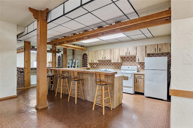 kitchen featuring a kitchen bar, tasteful backsplash, kitchen peninsula, white appliances, and a drop ceiling