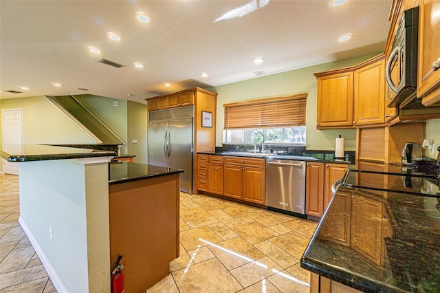 kitchen featuring dark stone counters, stainless steel appliances, a kitchen island, and sink