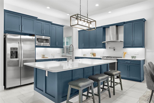 kitchen featuring wall chimney range hood, a center island with sink, stainless steel appliances, a kitchen breakfast bar, and blue cabinets