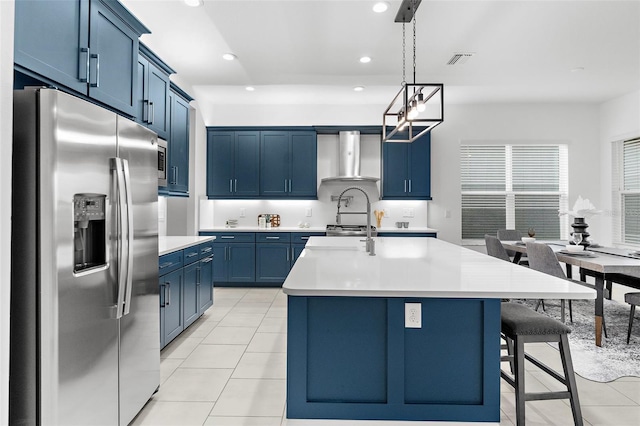 kitchen with stainless steel fridge with ice dispenser, an island with sink, light tile patterned floors, pendant lighting, and wall chimney range hood