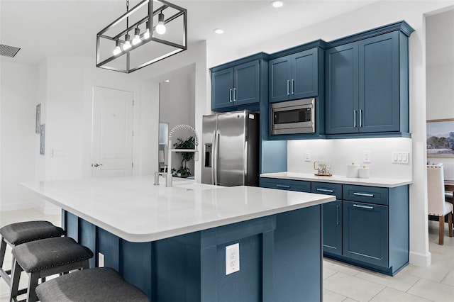 kitchen with stainless steel appliances, a center island with sink, blue cabinets, and hanging light fixtures