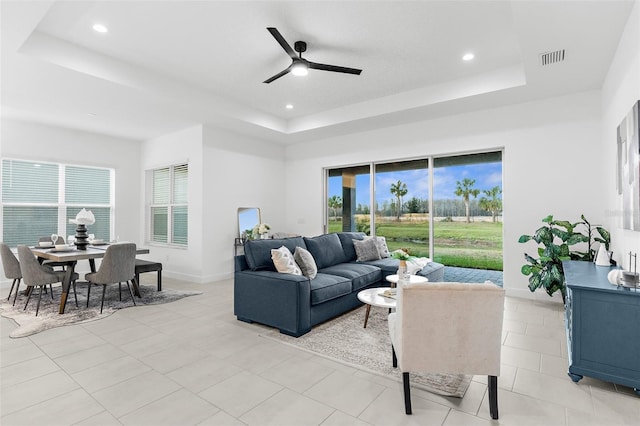 tiled living room with ceiling fan and a tray ceiling