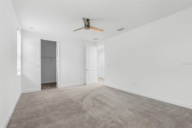 unfurnished bedroom featuring ceiling fan, a spacious closet, a closet, and light carpet