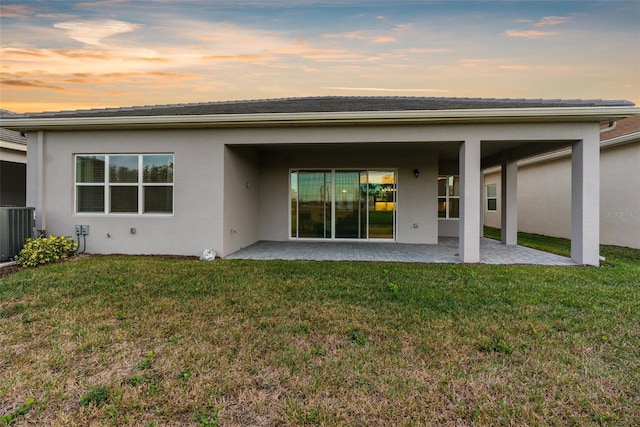 back house at dusk with central air condition unit, a lawn, and a patio