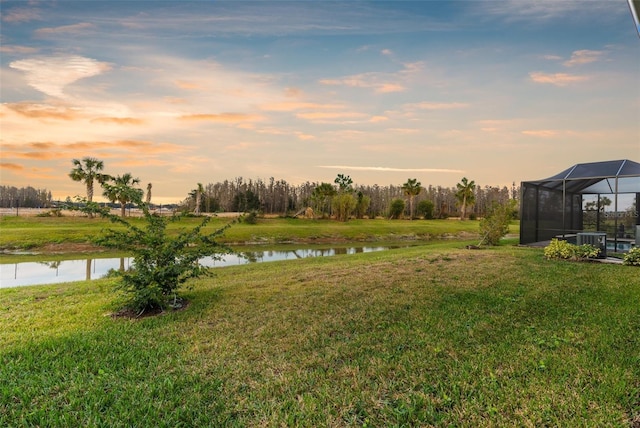 yard at dusk with a water view and glass enclosure