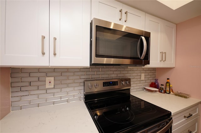 kitchen with light stone counters, decorative backsplash, stainless steel appliances, and white cabinets